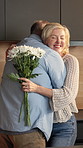 Flowers, happy and old couple hug in kitchen for surprise, gratitude and gift for love in home. Marriage, smile and man and woman with bouquet, present and embrace for affection, trust and connection