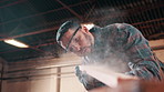 Carpenter, man and blow dust with plank in workshop, furniture manufacturing or production process. Woodwork, person and remove sawdust, craftsmanship and wipe shavings to clean in carpentry industry