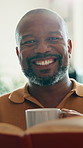 Coffee, face and reading book with smile of black man in home living room for literature hobby. Beverage, happy and story with mature person in apartment for fantasy or fiction novel on weekend