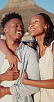 Laugh, black couple and hug with view on beach for romantic getaway, sightseeing and scenery. Vacation, love and happy people with pointing outdoor for exploring, conversation or healthy relationship