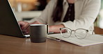 Student, hands and typing in home with laptop, glasses and notebook for distance learning university. Woman, research and study in house with computer, coffee or online education for college project.
