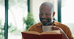 Funny, black man and reading book in home with tea, relax and literature on weekend in morning. Novel, drink or mature person at living room apartment for information, happiness or laugh at story