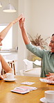 Mature, women and playing cards in home with high five, winner talk and laugh for bonding together. Happy friends, game victory and celebration in house with contest win, support or social gathering.
