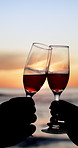Drinks, toast and hands of couple by beach for celebration, anniversary and bonding on vacation. Travel, sunset and people with alcohol, glass and cheers for love, commitment and relationship by sea