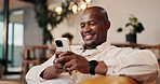 Smile, black man and relax in home with phone, social media and browsing website in living room. Happy, male person or reading at house with mobile, communication and download ebook for weekend break