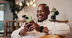 Smile, black man and rest in home with phone, social media and browsing website in living room. Male person, laugh and reading at house with mobile, communication and download ebook for weekend break