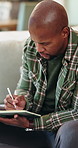 Sofa, writing or black man with book for remote work, schedule or checking tasks in home. Male person, freelancer or planning with diary, laptop or notebook for information, agenda or report in house