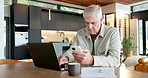 Typing, phone and laptop with old man in kitchen for social media, ebook subscription and relax. Online taxes, retirement and mature person in home, tech for communication and finance planning