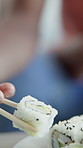 Hands, person and sushi at restaurant with chopsticks, culinary and seafood cuisine for lunch. Closeup, customer and Japanese dish for nutrition, gourmet appetizer and raw fish for authentic delicacy