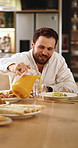 Happy, man and food with orange juice in home for vitamin C, health or wellness at dinner table. Male person, smile or pouring with glass, snack or drink for beverage, meal or liquid fruit in house