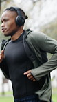 Fitness, man or running with headphones at park for exercise, pace training or music playlist. Runner, black person or workout in nature with audio streaming, endurance challenge or physical activity