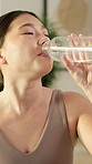 Health, drinking and woman with water in home for fitness, wellness or diet on weekend by yoga mat. Break, relax and Asian female person with beverage in bottle for hydration in living room at house.