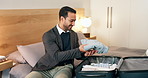 Man, suitcase and unpacking on bed for business travel, stay or accommodation in hotel or resort. Happy, male person or luggage with clothes in bedroom for commute or company relocation in apartment