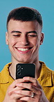 Happy man, phone and laugh in studio for funny joke, social media or meme. Male student, reading and smile on mobile tech for networking, chatting or message or communication on blue background