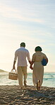 Couple, holding hands and adventure with picnic basket at beach, back or summer holiday with partner. Outdoor, people and walk with spouse on coastal vacation, space and marriage commitment in nature