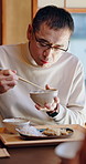 Asian man, eating and food in home with chopsticks, healthy rice and traditional meal for lunch. Mature person, bowl and utensils in lounge for brunch, nutrition snack and authentic Chinese cuisine