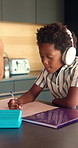 Headphones, writing and child in kitchen for homework with listening to music at house with book. Audio tech, student and boy kid studying for mathematics quiz for development, growth or education.