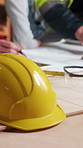 Hands, architect and drawing at site with helmet, blueprint and illustration for architecture ppe. People, writing and safety hard hat at workshop with paperwork, floor plan and structure of building