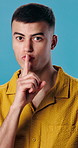 Man, face or lips with secret in studio for silence, quiet or confidential on a blue background. Portrait, male person or rumor with private information for gossip, mysterious plan or plotting scheme