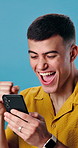 Man, promotion and shocked with phone in studio for good news, winning prize or deal. Happy, excited person or omg with fist pump and smile on tech for online offer, special sale and blue background