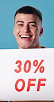 Sale, face and man in studio with poster, announcement and advertising for retail discount. Happy, portrait and person with sign for deal, promotion and shopping news for bargain on blue background