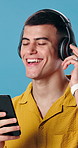 Dance, happy and man with headphones in studio for good mood, positivity and energy with phone. Relax, dancer and person with mobile app for streaming music, playlist and radio on blue background