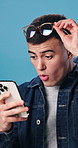 Surprise, phone and man in studio with good news, update or notification of winning gambling. Prize, shock and person with cellphone for financial bonus with online competition by blue background.