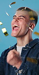 Celebration, confetti and studio with happy man for winning or achievement on a blue background. Excited, male person or success with smile or fist pump for promotion, discount or lottery prize