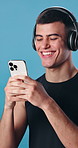 Man, phone and message in studio with fitness, headphones and typing for workout. Happy athlete, texting and tech with laugh for exercise, streaming podcast or music with app on blue background
