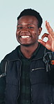Travel, face and black man with perfection in studio for good adventure or sightseeing on a blue background. Portrait, male person or traveler with smile, backpack or OK sign for perfect review