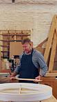 Carpenter, workshop and man with wood, discussion or joinery accuracy for production with team. Woodwork, talking or mature person with piece for planning, furniture manufacturing or carpentry tools