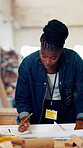 Architecture, black woman and writing on blueprint in workshop with wood, notes and layout for process. Construction, woodwork and manufacturing in factory for floor plan, project and idea for design