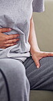 Menstruation, sore and hands in house with massage, discomfort and stomach ache in period symptoms. Health, cramps and woman on sofa with belly rub, endometriosis and soothe abdominal pain on cycle.