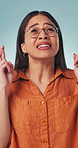 Hope, fingers crossed and woman in studio with wish on university acceptance for education. Glasses, person and student with miracle or good luck gesture for college results on blue background.
