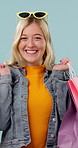 Face, girl and excited with shopping bags in studio for retail discount, sale celebration or spree. Shopper, person or happy with gifts on blue background for fashion deal, rewards program or bargain