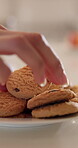 Cookie, hand and plate on counter in home kitchen for eating, hungry or sweet treat at breakfast. Biscuit, closeup and food with person in apartment for confectionery snack, dessert or unhealthy diet