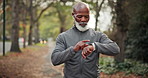 Black man, smart watch and earphones at park for fitness, streaming and podcast for exercise. Mature person, reading and wristwatch in nature for training, listening to music and physical activity