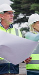 Engineering, team and walk at construction site with blueprint, property inspection and conversation. Mature people, talk and document outdoor for building design, engineer opinion and collaboration.