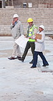 Civil engineer, team and walking with radio on construction site, communication or inspection update. Architect, discussion and mature people with blueprint, project management and talking with tech