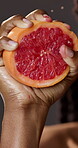Hands, squeeze and person with grapefruit in studio for wellness, healthy diet and vitamin c. Dark background, hydration and woman with fruit for nutrition, clean eating and antioxidants for detox