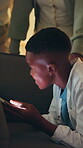 Discreet, night and phone with black child on sofa in home living room to hide from parents. Late, screen time and social media with sneaky boy in apartment for stealthy browsing on mobile app