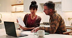 Couple, conversation and documents in home with laptop, financial planning or mortgage loan proposal. Married, mature people and talk in kitchen with paperwork, debt financing and check credit score.