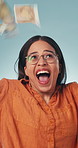 Excited, woman and money rain in studio for win, financial freedom and success on blue background. Cash fall, happy person and lottery celebration with reward, rich or jackpot with wealth achievement