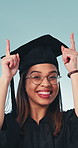 Face, graduation and woman with achievement, pointing up and opportunity promotion in studio. Portrait, excited person and hand gesture for education, celebration and success on blue background
