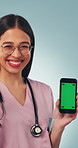 Nurse, face and woman with phone, green screen and presentation for telehealth app or recommendation. Blue background, medical expert and happy person with mobile, mockup space and pointing in studio