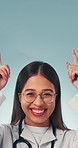 Doctor, face and woman with smile, marketing and advice for healthcare services and offer in studio. Blue background, medical professional and happy person with health tips, dance and point at space
