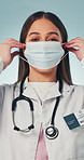 Face, healthcare and doctor in studio with mask for tutorial, safety compliance and prevention. Portrait, happy and woman wink with ppe for hospital wellness, protection or hygiene on blue background