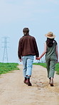 Walking, holding hands and back of couple in countryside for bonding, travel and holiday together. Love, dating and man with woman on dirt trail for fresh air, wellness and explore on weekend getaway