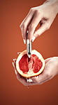 Hands, grapefruit and erotic toys in studio with liquid dripping, tutorial and how to pleasure woman. Person, sensual product and demonstration with fruit, sex education or wellness on red background
