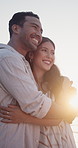Happy, couple and hug by beach with summer holiday, loyalty and travel together for romantic getaway. Flare, people dating and embrace outdoor by ocean with love, relationship and smile for vacation.